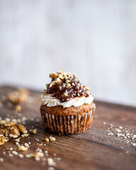 Tasty chocolate muffin with creme mascarpone and chocolate on top, covered with nuts. Placed on wooden desk. Sweet fresh and homemade cupcake.