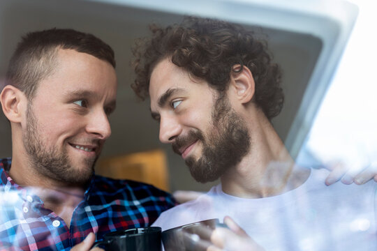 Young Gay Couple In Love Looking Out The Window. Two Young Androgynous Men Smiling Together And Having Coffee.