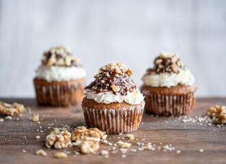 Tasty chocolate muffin with creme mascarpone and chocolate on top, covered with nuts. Placed on wooden desk. Sweet fresh and homemade cupcake.
