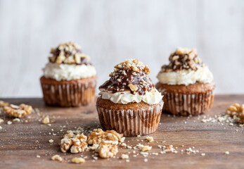 Tasty chocolate muffin with creme mascarpone and chocolate on top, covered with nuts. Placed on wooden desk. Sweet fresh and homemade cupcake.