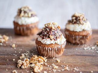 Tasty chocolate muffin with creme mascarpone and chocolate on top, covered with nuts. Placed on wooden desk. Sweet fresh and homemade cupcake.