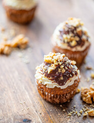 Tasty chocolate muffin with creme mascarpone and chocolate on top, covered with nuts. Placed on wooden desk. Sweet fresh and homemade cupcake.