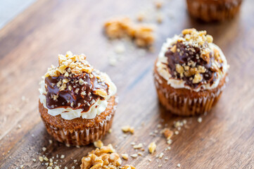 Tasty chocolate muffin with creme mascarpone and chocolate on top, covered with nuts. Placed on wooden desk. Sweet fresh and homemade cupcake.