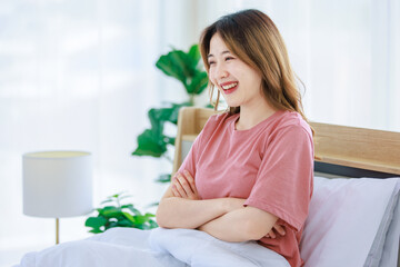 Obraz na płótnie Canvas Millennial Asian young happy cheerful female teenager sitting laying smiling on pillow under thick warm blanket on cozy bed in bedroom at home in morning