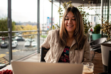 Young mexican woman chatting with friends and enjoying her morning coffee on the terrace of modern cafe before working day. Morning routine, mental health, wellness and slow living