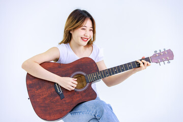 Fototapeta premium Isolated cutout studio full body shot of Millennial Asian young happy cheerful female teenager teen model in casual outfit sitting on square box smiling singing playing guitar on white background