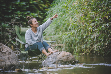 Young woman sitting on camping chair in stream for relax