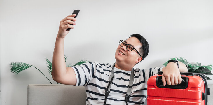 Happy Asian traveler man glasses selfie on smartphone with luggage
