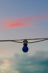 Low angle view of dark blue lamp hanging outdoors from an electric light cord against evening sky.
