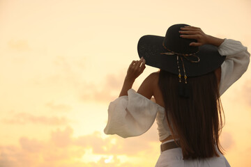 Young woman in hat at sunset, back view. Space for text