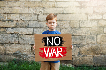 Sad boy holding poster with words No War against brick wall outdoors © New Africa