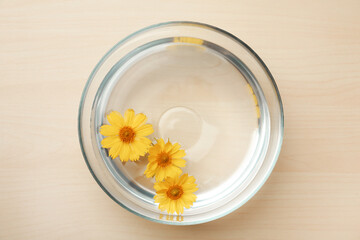 Glass bowl with water and yellow flowers on wooden table, top view