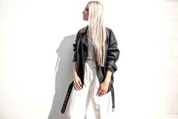 Fototapeta premium A beautiful girl with long even hair walks around the city, the model is wearing a black braid and white trousers