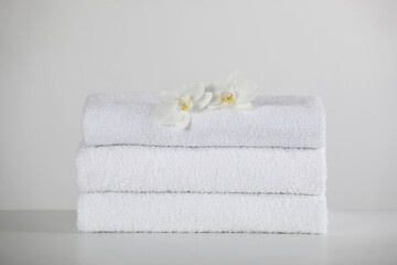 Obraz na płótnie Canvas Soft folded towels and orchid flowers on white table