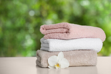 Stacked towels with flower on white table against blurred background, space for text
