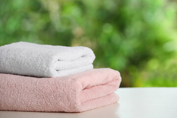 Folded towels on white table against blurred background, space for text