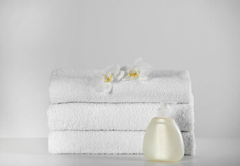 Fototapeta na wymiar Soft folded towels, orchid flowers and dispenser on white table