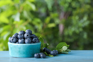 Tasty fresh blueberries and green leaves on blue wooden table outdoors, space for text