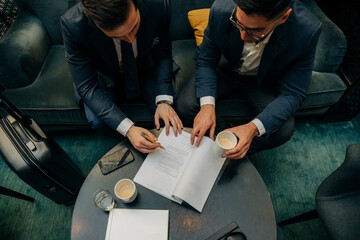 High angle view of young businessman signing contract by male colleague in hotel lounge