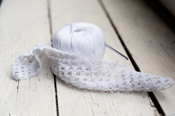 crocheted fabric is wrapped around  ball of white thread. Still life in a vintage wooden table