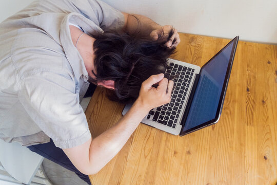 Frustrated man lying on a laptop with a blank screen tearing his hair out, clenching his fingers into a fist. copy space. top view - Powered by Adobe