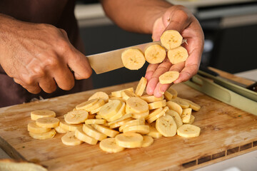 Unrecognizable young african man cutting plantains in a kitchen.