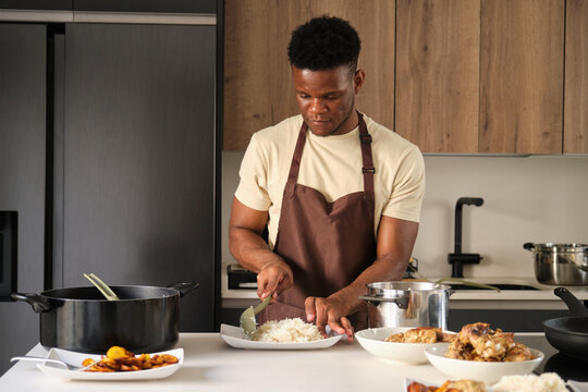 Young black man serving rice on a plate in a kitchen.