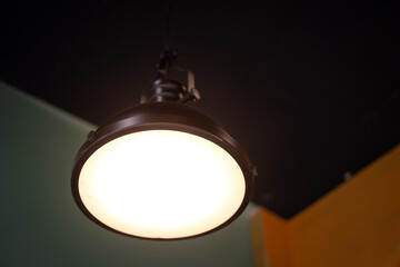 A metallic ceiling lighting lamp is glowing with yellow warm light shade. Interior decoration object equipment photo. Selective focus.