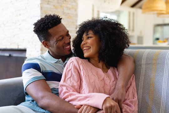 Happy african american couple sitting on sofa in living room, embracing and smiling