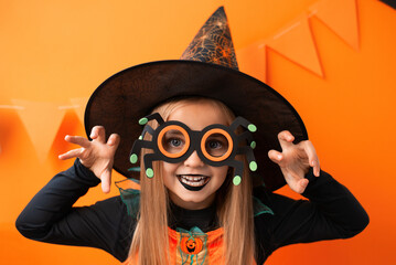Portrait of an angry little girl in a witch costume on an orange background. Happy Halloween