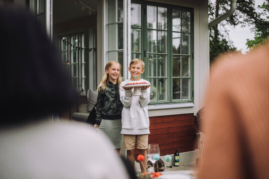 Boy holding cake while standing with female sibling near doorway