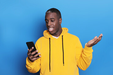 Fototapeta premium Young black man over isolated blue background sending a message with the mobile