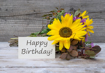 Birthday card with the English text: Happy Birthday is in front of an autumn bouquet with sunflowers.