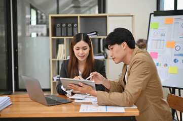 Charming Asian businesswoman looking at tablet screen, working with her male boss