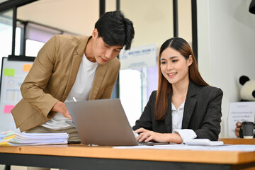 Fototapeta premium Asian businesswoman working on her project on laptop while discussing with her male colleague