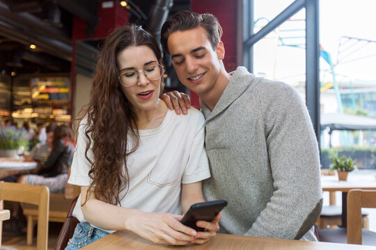 Handsome young couple having fun looking smartphone in bar cafe restaurant