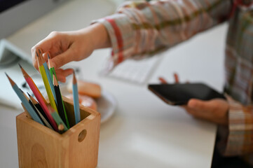 Close-up, A female graphic designer in a flannel shirt choosing color pencil for her artwork