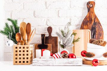 Front view of eco-friendly wooden kitchen utensils and Christmas decorations in a wooden box on a white wooden table against a brick wall.