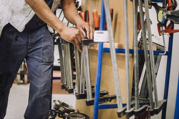 Male carpenter arranging work tools on rack while working in workshop