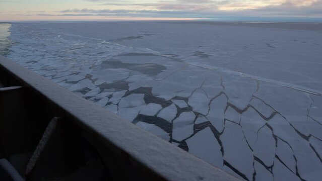 Ice on water. View back to ship's railing at stern of vessel. A wave on surface shakes ice floes. Ice was split into pieces along side of ship