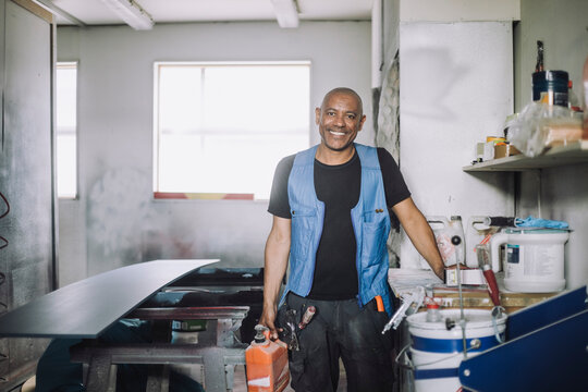 Portrait of smiling bald painter standing by workbench at workshop