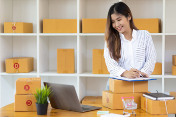 Startup SME small business entrepreneur of freelance Asian woman using laptop and box to receive and review orders online to prepare to pack sell to customers, online sme business ideas.