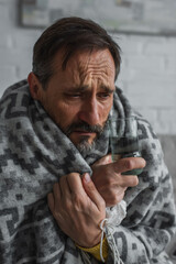 diseased man wrapped in warm blanket holding glass of water.