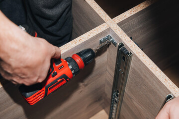 Close-up of male hands with a red screwdriver while assembling a cabinet. View from above,...