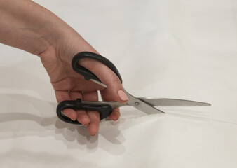 A woman holds scissors in her hands to cut the wallpaper on the wall. a woman's hand holds a pair of scissors in close-up. Scissors cut paper.