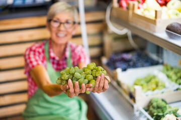 Woman works in fruits and vegetables shop. She is examining grapes.