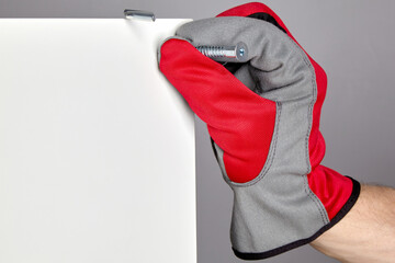 A hand in a red protective glove inserts a confirmation into a hole in a furniture shield. Assembly and repair of furniture