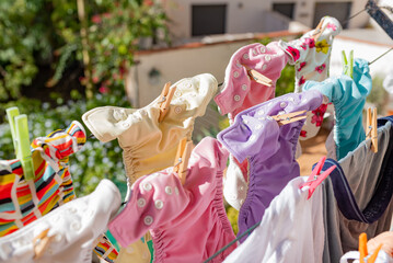 Cloth diapers hanging while drying under the sun on clothesline. Laundry of colorful reusable nappies for babies. - obrazy, fototapety, plakaty