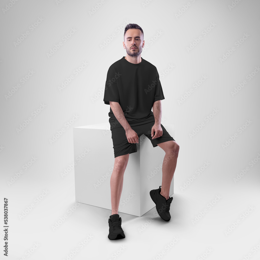 Wall mural isolated mockup of trendy black men's oversized t-shirt with shorts on man sitting on cube. - Wall murals