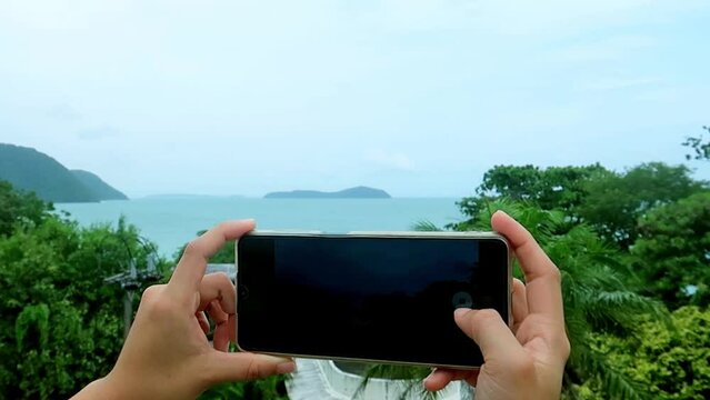 Hands holding smartphone taking ocean view picture 